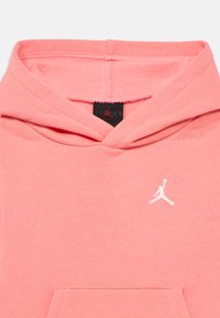 Ροζ βαμβακερό φούτερ με κουκούλα και κορδόνια, τσέπη καγκουρό και λευκό λογότυπο Jumpman στο στήθος. Μαλακή υφή με εμφανείς ραφές.