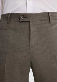 Brązowe spodnie w kratę wykonane z fakturowanej tkaniny, zapinane na jeden guzik, z bocznymi kieszeniami. Dopasowany krój.