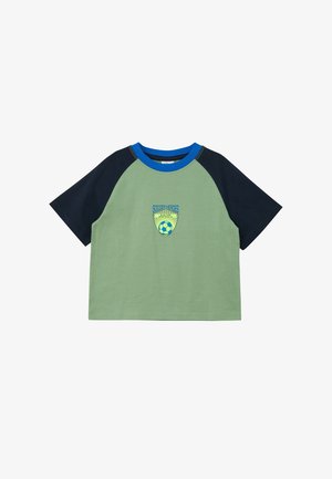 Camiseta raglán de manga corta para niños con cuerpo verde, mangas azul marino, cuello azul y logo "Héroes del Fútbol" con balón de fútbol en el frente.