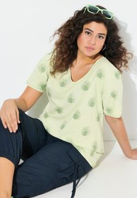 Camiseta de cuello en V verde claro con estampados de hojas, combinada con pantalones cargo oscuros de color navy. Textura suave, mangas cortas, ajuste relajado.