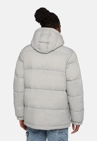 Puffjacka i ljusgrått, med huva, kviltad design och elastiska ärmslut. Mjuk, slät textur med horisontella sömnadsdetaljer.