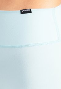 Ljusblå sömlösa leggings med en slät yta, utrustade med en svart etikett med varumärkesnamnet "SMILODOX" nära midjebandet.