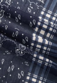 Blått stoff med paisley- og blomsterdesign sammen med rutete mønstre. Teksturert overflate med kontrasterende hvite detaljer.