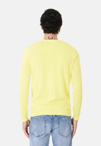 Maglione giallo a maniche lunghe in tessuto morbido, con scollatura rotonda e polsini a costine, abbinato a jeans azzurri chiari.
