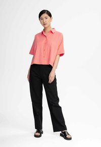 Koraalrood kortmouw overhemd met knopen en gestructureerde stof, gecombineerd met zwarte wijde broek en zwarte platte sandals. Eenvoudig ontwerp, losse pasvorm.