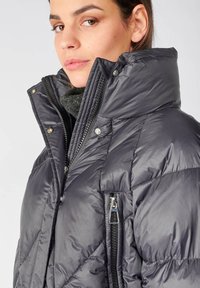 Giacca puffer grigio scuro con colletto alto, caratterizzata da un design trapuntato, chiusura frontale con zip e tasche laterali con dettagli metallici.