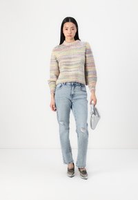 Pull en tricot avec des rayures multicolores dans des teintes pastel, col et poignets côtelés. Porté avec un jean bleu clair déchiré et un sac argenté.