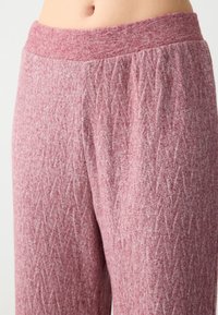 Różowe dzianinowe spodnie z teksturowanym wzorem w diamenty oraz elastycznym paskiem w talii. Materiał wydaje się miękki i ma lekki połysk.