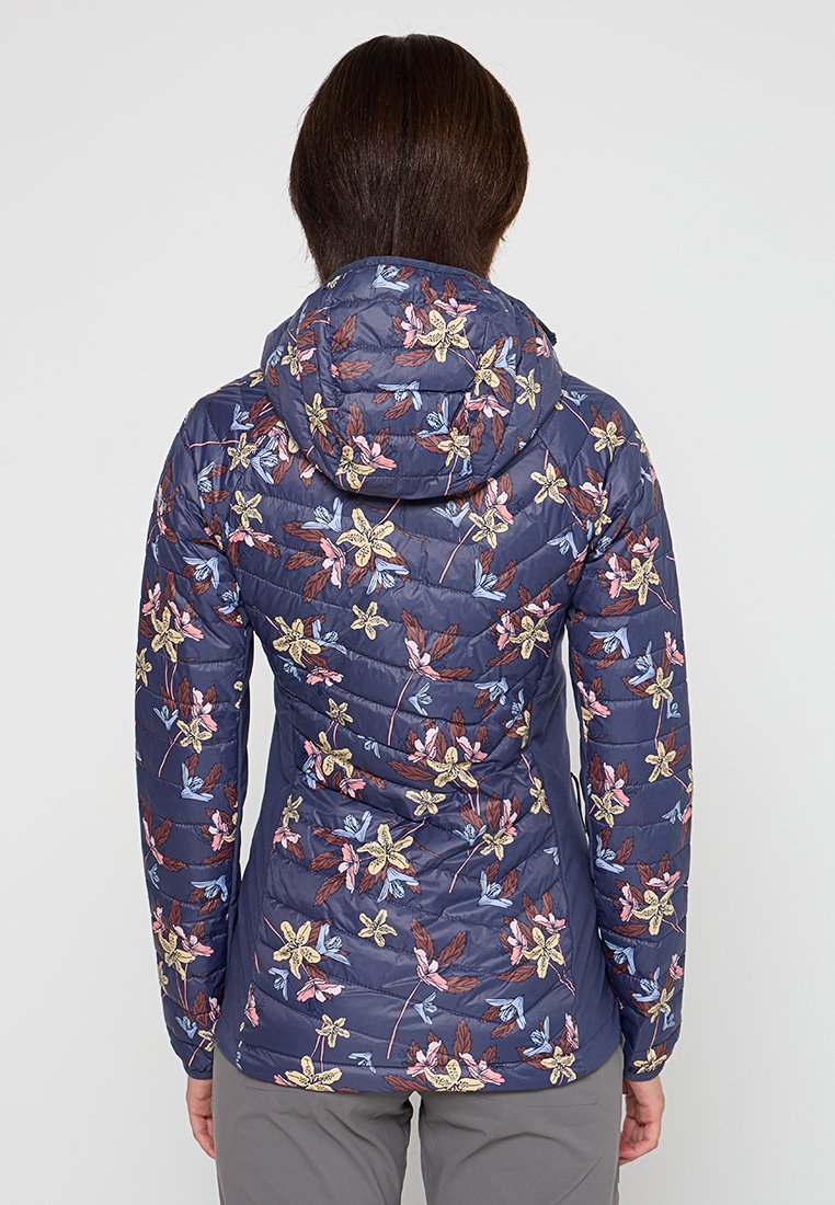 Chaqueta acolchada navy con patrón floral, textura acolchada, silueta ajustada y capucha. Acentos florales en tonos rosa, azul y amarillo.