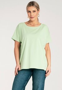 Jasnozielona koszulka z krótkim rękawem o szerokim dekolcie, miękka w dotyku i luźna, w połączeniu z niebieskimi dżinsami.