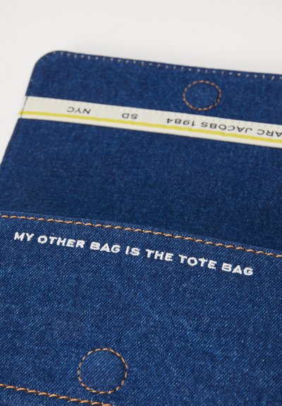 Geantă din denim cu text alb care spune "GEANTA MEA CEA ALTĂ ESTE GEANTA TOTE." Prezintă o cusătură portocalie și un accent circular în partea de sus.