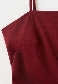Robe sans manches en tissu texturé rouge profond avec fines bretelles et encolure droite sur fond blanc.