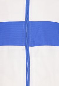 Bílá a modrá bunda na zip; má výraznou modrou pruh, texturovanou tkaninu a centrální zip s modrým detailem.