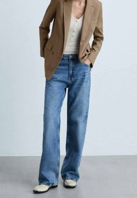 High-waisted, wide-leg blue jeans made of denim. Paired with a cream tank top and a brown blazer. Textured fabric and tailored fit.