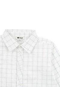 Camicia bianca a quadri in tessuto leggero. Presenta un colletto classico, chiusura con bottoni e un sottile motivo a griglia blu. Etichetta del marchio visibile.