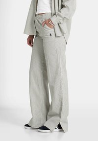 Gestreepte wijde broek van lichtgroene en witte stof met een elastische tailleband en zijzakken, met een grafisch detail op de zak.
