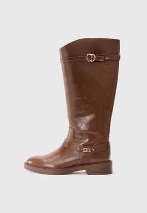 Botte d'équitation haute en cuir marron avec un talon bas et des brides décoratives à boucle dorée autour de la cheville et de la tige supérieure.