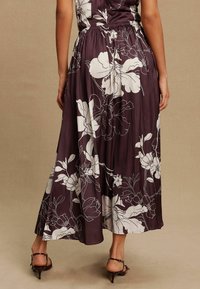 Langes lila Blumenkleid mit tailliertem Schnitt, versehen mit weißen Blumenmustern, glatter Textur und einem schwingenden Rock. Inklusive High-Heelsandalen.