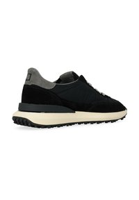 Sneaker nera in suede e tessuto con un accento grigio, dotata di una suola in gomma testurizzata e lacci piatti. Vista laterale mostrata.