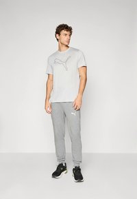 Grå bomull t-skjorte med svart Puma-logo, kombinert med matchende grå joggebukser med en liten hvit logo, brukt sammen med svarte sportssko.