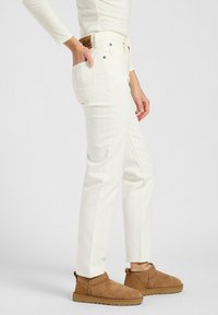 Jeans de denim blanco con corte recto, que cuentan con un diseño estándar de cinco bolsillos y una etiqueta de cuero marrón con la marca en la parte trasera.