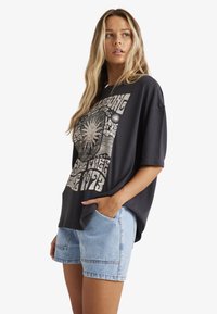 Sort oversized t-shirt med metallisk grafisk print og korte ærmer, parret med lyseblå denimshorts med sidelommer.