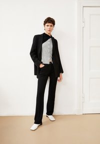 Zwarte oversized blazer over een grijze cropped button-up, gecombineerd met zwart op maat gemaakte broek en witte schoenen. Gladde stof en strakke lijnen.
