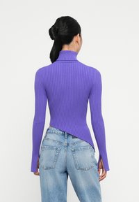 Maglione a collo alto ribbed viola con maniche lunghe, caratterizzato da un orlo asimmetrico e una finitura testurizzata, abbinato a jeans azzurri chiari.