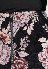 Jupe noire à motifs floraux avec un détail de fermeture éclair, un tissu texturé et des motifs complexes de fleurs roses et rouges avec des feuilles vertes.