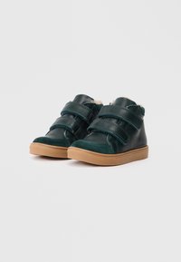 Grüne Leder- und Wildleder-Halbschuhe mit zwei Klettverschlüssen, weichem Innenfutter und brauner Gummisohle. Glatte und strukturierte Oberflächen.