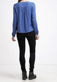 Blue long-sleeve blouse with a round neckline and a pleated back, paired with black skinny jeans and black ankle boots.