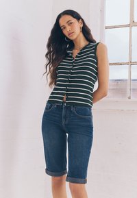 Top verde cu dungi, fără mâneci, cu nasturi, asortat cu pantaloni scurți din denim închis, cu tivuri întoarse. Design simplu, croială lejeră și material texturat.