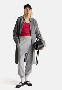 Szary wełniany płaszcz na czerwonym topie crop, szare dresy i czarne buty. Uzupełniony czarną torebką i czapką. Widoczne białe skarpetki.