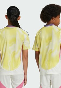 Due bambini indossano maglie leggere a maniche corte. Le maglie presentano un design astratto giallo, rosa e bianco con texture a rete.
