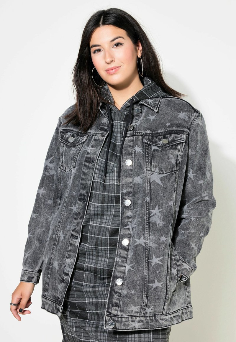 Denimjack in vervaagd zwart met sterpatronen, voorzakken en zilverkleurige hardware, gecombineerd met een geruite hoodie eronder.