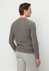 Maglione grigio a maglia texturizzata con maniche lunghe e orlo a coste, visto da dietro, abbinato a pantaloni grigi chiari.