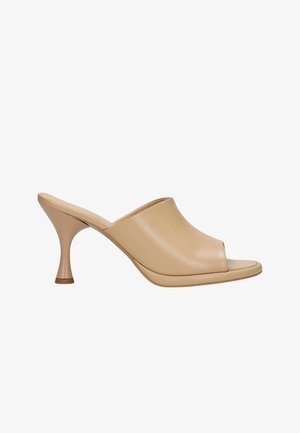 Mules beiges à bout ouvert avec une tige en cuir lisse, un côté cintré et un talon effilé. Le talon présente un petit accent doré à la base.