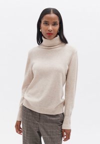 Beige Rollkragenpullover aus weichem Material mit langen Ärmeln, einer taillierten Passform und gerippten Akzenten an den Bündchen und dem Saum.
