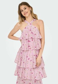 Rózsaszín, réteges ruha könnyű anyagból, virágmintákkal. Keresztbe futó pántokkal és fodros rétegekkel rendelkezik, amelyek textúrát adnak neki.