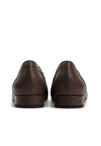 Para ciemnobrązowych, teksturowanych skórzanych mokasynów widzianych od tyłu, spoczywających na białej powierzchni, z niskimi obcasami i widocznym przeszyciem.