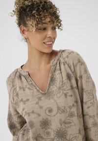 Bluză bej cu decolteu în V, având broderie florală complexă în fir închis și țesătură moale, texturată. Croi lejer, cu umeri strânși.