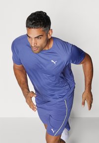 T-shirt e calções desportivos roxos com logótipo branco, apresentando um tecido texturado e um design ajustado, ideal para desporto e vestuário ativo.