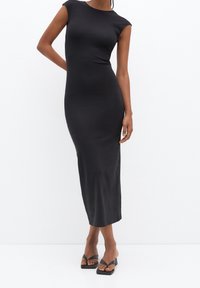 Robe midi noire ajustée avec des manches courtes et un col rond. Fabriquée en tissu lisse, elle présente une silhouette élégante et une fente sur le côté. À associer avec des sandales à talons carrés.