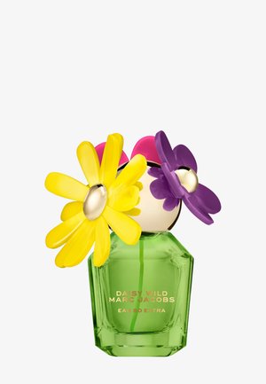 Flacon de parfum en verre vert portant l'étiquette "Daisy Wild Marc Jacobs Eau So Extra", surmonté de grands capuchons en plastique en forme de fleurs jaunes et violettes.