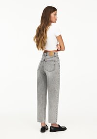 Lichtgrijze high-waisted jeans met een losse pasvorm, rechte pijpen en zichtbare stikdetails. Gepaard met zwarte schoenen en een witte top.