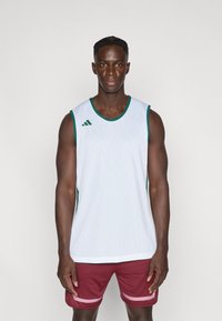 White athletic tank top with green accents and Adidas logo; made from mesh material. Worn with maroon shorts featuring pink stripes.