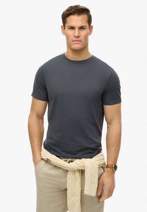 Camiseta corta de manga corta gris oscuro con cuello redondo, combinada con pantalones beige claros y un suéter de punto color crema atado a la cintura.