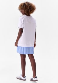 Witte top met korte mouwen en een naaddetail aan de achterkant, gecombineerd met een lichtblauwe geplooide rok met dunne verticale strepen en zwart-witte sneakers.