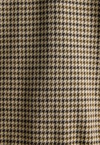 Houndstooth fabric in beige and brown tones, featuring a symmetrical pattern, with a soft texture and a woven finish.