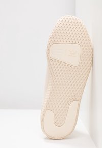 Beige Adidas sneakersula med texturerat grepp, Michael Williams samarbetslogotyp, lutande mot en vit yta.